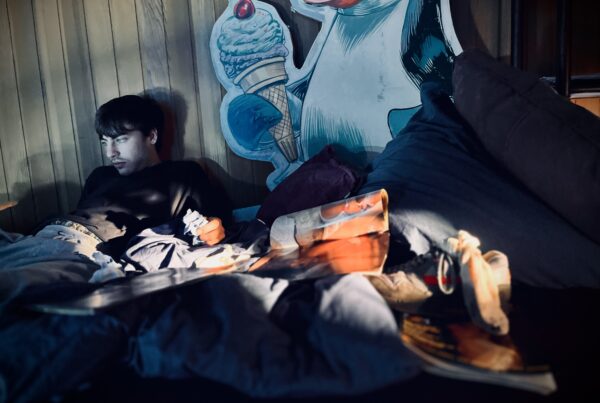 Who Could Have Seen This C_ming? (2026) - set design with moody retro interior, old magazines and beautiful light reflections, young man looking delusional but in a comical way