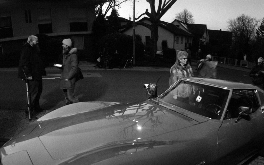 Picobello (2026) – Behind the Scenes Still - production design Picobello (2026) – Production Design for short film, production designer Jan Christoph Scheurer and director talking beside Corvette Stingray, black-and-white on-set moment
