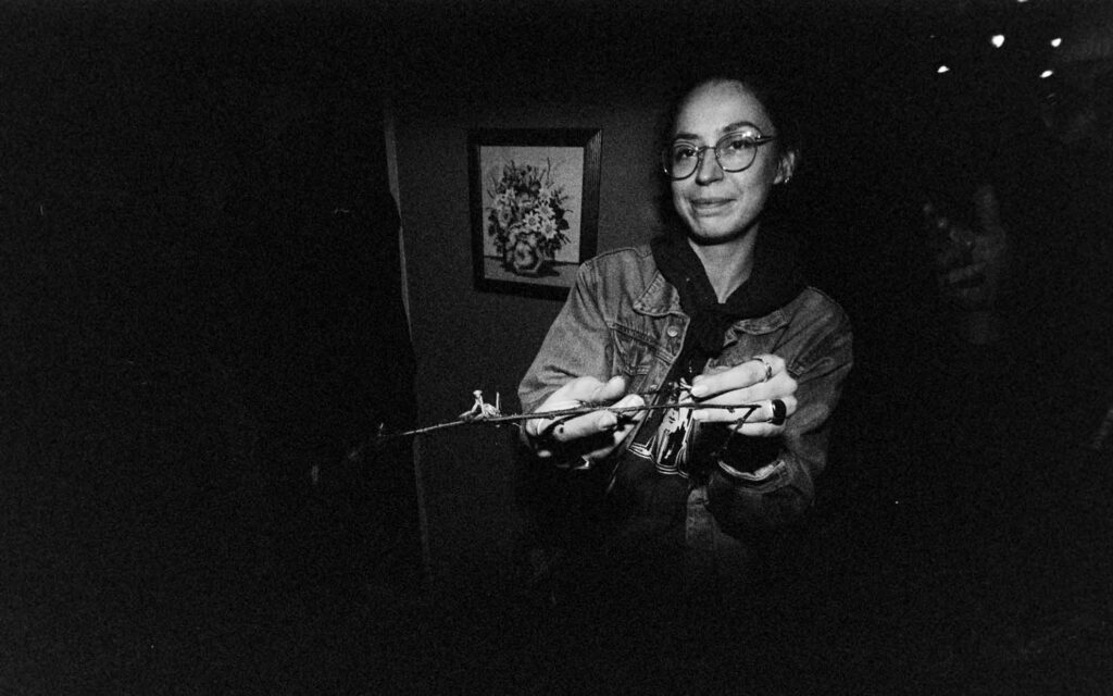 Picobello (2026) – Behind the Scenes Still - production design Picobello (2026) – Production Design for short film, assistant carefully holding a praying mantis, dark candid moment, intimate behind-the-scenes atmosphere