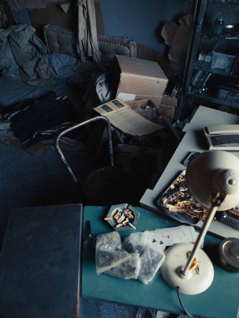 Picobello (2026) – Behind the Scenes Still - production design Picobello (2026) – Production Design for short film, cluttered desk with tools, retro lamp and jars, plastic sheets, moody window light, tense and dark mood