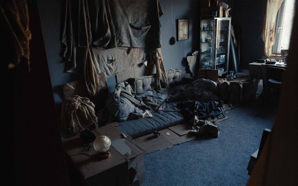 Picobello (2022) – Behind the Scenes Still - production design Picobello (2026) – Production Design for short film, dark, moody room with improvised bed of blankets and cardboard, eerie and mysterious atmosphere.