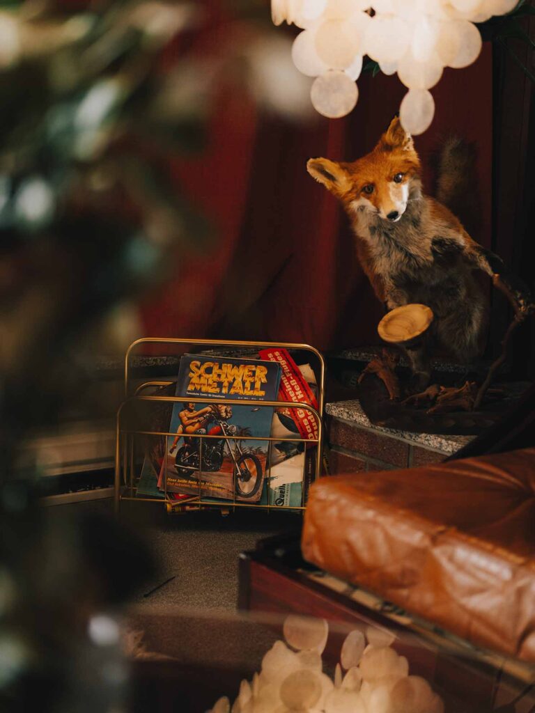 Picobello (2022) – Behind the Scenes Still - production design Picobello (2022) – Production Design for short film, stuffed fox on ledge, warm red drapes, vintage magazines, soft lamp glow, 70s interior mood