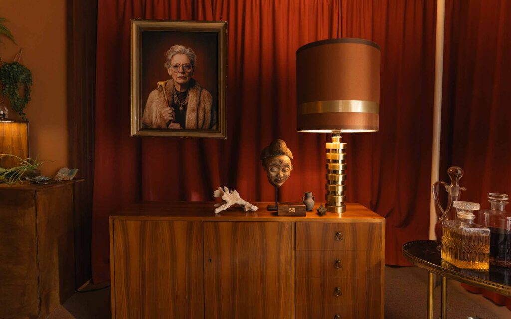 Picobello (2022) – Behind the Scenes Still - production design Picobello (2022) – Production Design for short film, red velvet drapes, mid-century sideboard, brass lamp, portrait, barware, warm cinematic glow, portrait of a female gangster boss