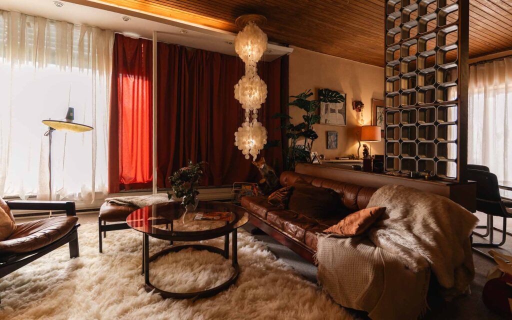 Picobello (2026) – Behind the Scenes Still - production design Picobello (2026) – Production Design for short film, warm mid-century living room with red curtains, shag rug, leather sofa, sculptural lamps and retro divider